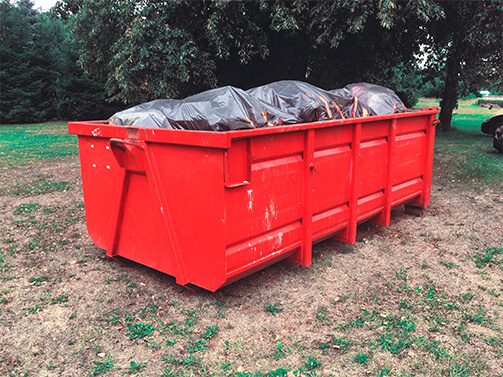 red dumpster filled with garbage bags